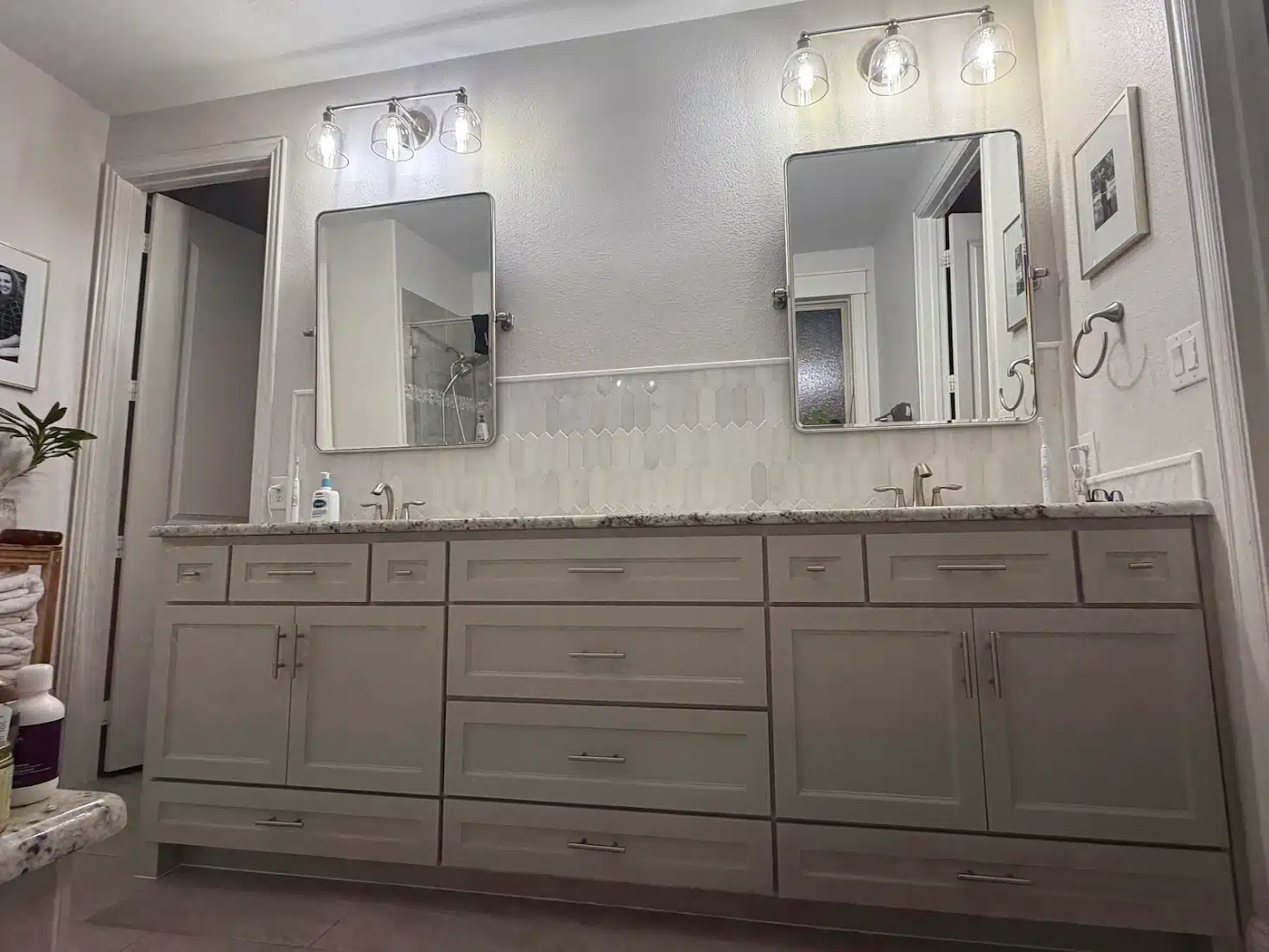 Custom double vanity The Colony TX featuring gray shaker cabinets, granite countertop, elongated hexagon picket tile backsplash, dual mirrors and brushed nickel hardware by I Love My Bathroom