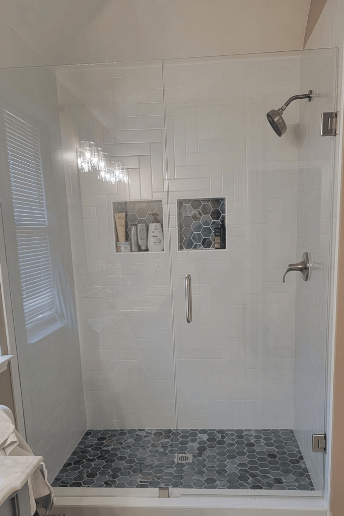 Custom walk-in shower with large white subway tile, hexagon mosaic floor, dual built-in niches, and frameless glass enclosure — Grapevine, TX bathroom remodel