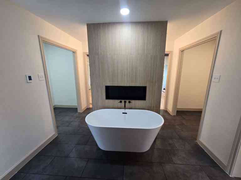 DFW bathroom remodeling FAQ — freestanding soaking tub with matte black wall mount filler, fluted tile accent wall, and large format dark floor tile by I Love My Bathroom Grapevine TX