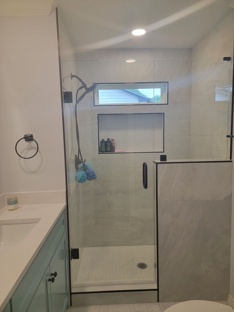 Full bathroom remodel Carrollton TX featuring sage teal vanity, frameless walk-in shower with large format porcelain tile, herringbone mosaic floor and matte black hardware by I Love My Bathroom