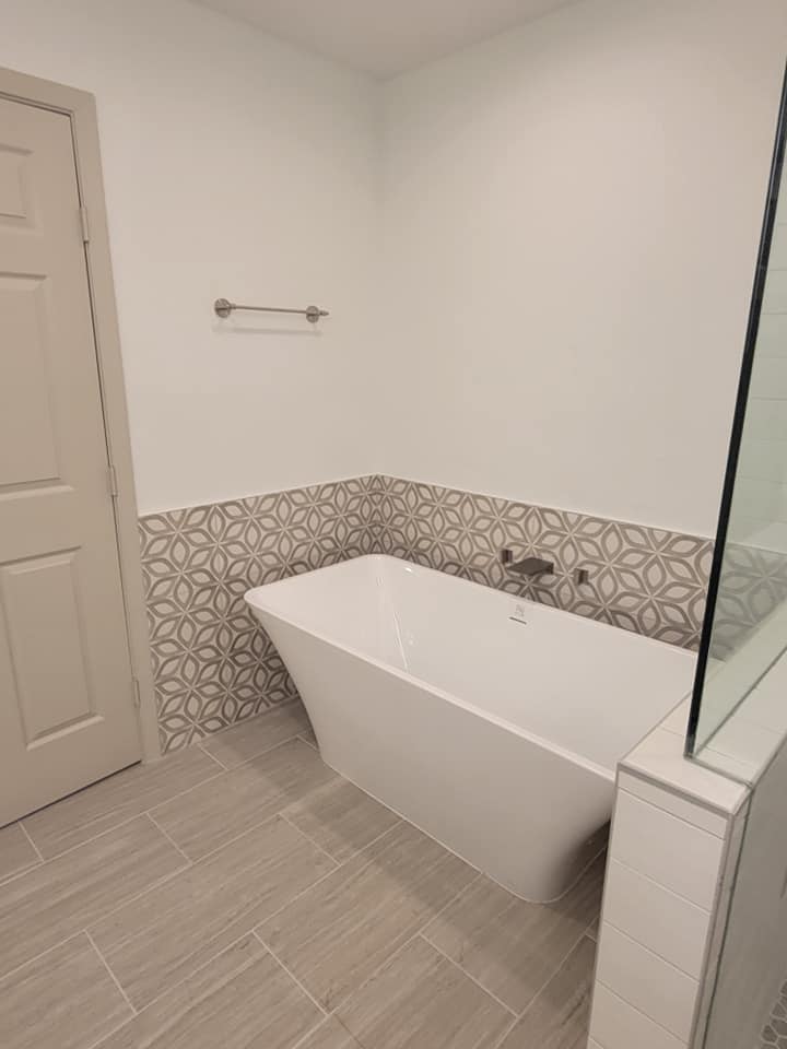 Master bath remodel Grapevine TX freestanding soaking tub with brushed nickel wall mount filler geometric tile half wall accent and wood look floor tile by I Love My Bathroom