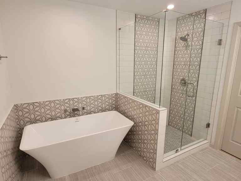 Master bath remodel Grapevine TX featuring freestanding soaking tub with wall mount filler geometric pattern tile accent wall walk-in shower with frameless glass and wood look floor tile by I Love My Bathroom