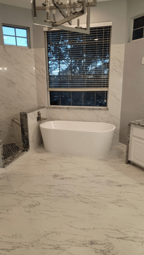 Master bath remodel Keller TX featuring freestanding soaking tub, floor to ceiling marble porcelain tile, large format marble floor tile, chandelier and brushed nickel wall mount filler by I Love My Bathroom