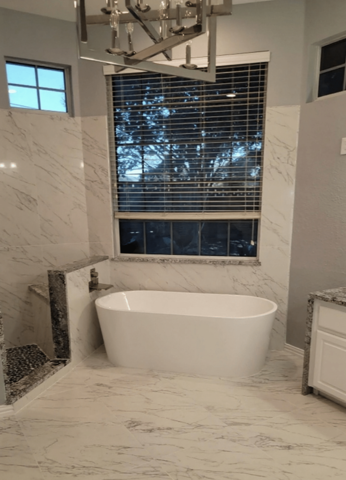 Master bath remodel Keller TX featuring freestanding soaking tub, floor to ceiling marble porcelain tile, large format marble floor tile, chandelier and brushed nickel wall mount filler by I Love My Bathroom