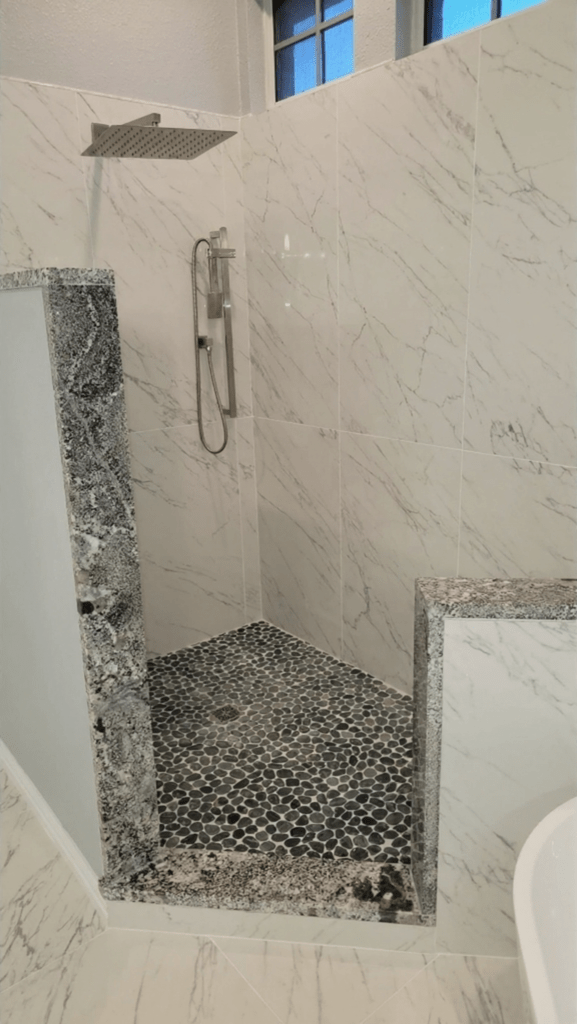 Master bath remodel Keller TX featuring marble porcelain shower tile, dark pebble mosaic floor, granite accent panels, square rain shower head and brushed nickel hardware by I Love My Bathroom