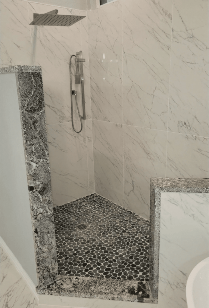 Master bathroom remodeling Keller TX featuring marble porcelain shower tile, dark pebble mosaic floor, granite accent panels, square rain shower head and brushed nickel hardware by I Love My Bathroom